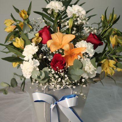 Centro floral con rosas rojas, liliums naranjas, claveles blancos, alstroemerias amarillas y eucalipto.